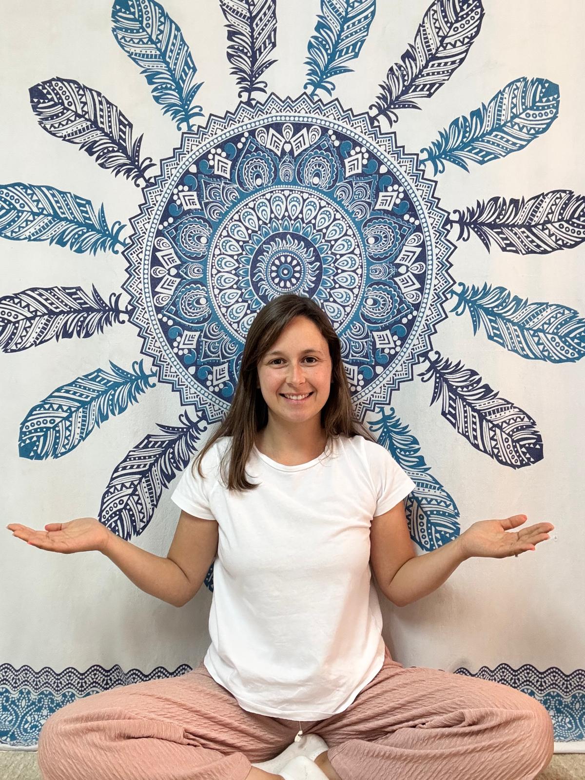 Retrato de Sara Rodrigues em posição de meditação, com as mãos abertas, contra um fundo de mandala azul